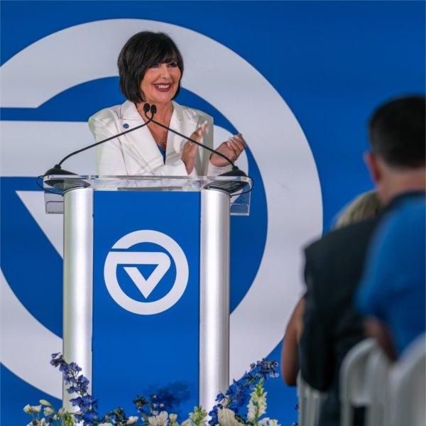 A person at a podium smiles while clapping. The podium and the backdrop both contain the Grand Valley State University logo.